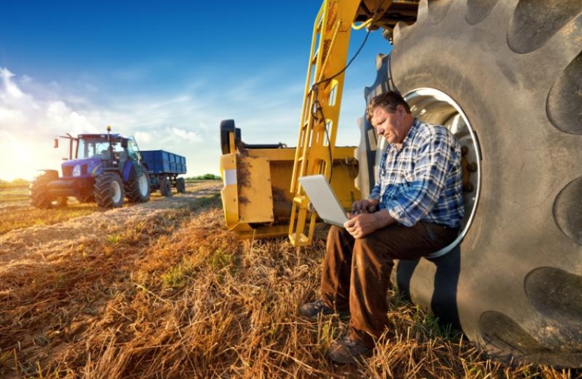 Farmer in a field with a laptop and a tractor in the background.